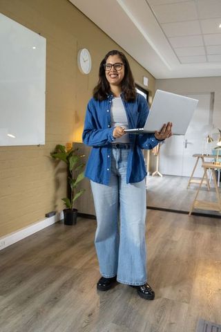 Smiling woman presenting with laptop in modern workspace classroom for collaborative learning