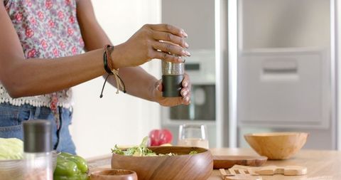 Woman Seasoning Fresh Salad in Modern Kitchen