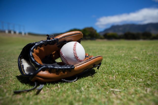 This image captures a close-up view of a baseball and glove resting on a grassy field under a clear blue sky. Ideal for use in sports-related content, outdoor activity promotions, summer event advertisements, or recreational activity blogs. The vibrant colors and natural setting evoke a sense of leisure and athleticism.