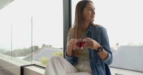 Young woman enjoying red tea by large window in minimalist apartment
