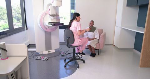 Female technologist consulting patient before mammogram using tablet in bright clinic