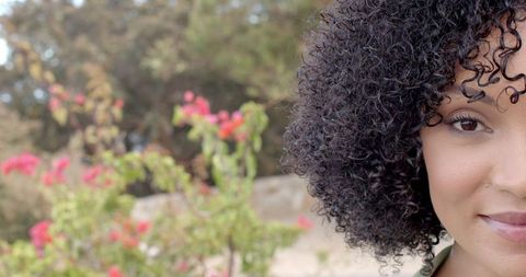 Smiling woman with curly hair enjoying vibrant garden scenery