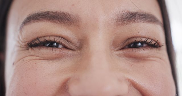 This image captures a close-up of a smiling woman's eyes, highlighting crow's feet wrinkles and long, beautiful eyelashes. The expression radiates joy and natural beauty. Suitable for use in articles or campaigns emphasizing aging gracefully, skincare, eye makeup, or emotional expressions and happiness.