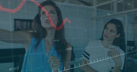 Two Women Pointing and Analyzing Falling Stock Chart on Glass Wall During Team Data Review