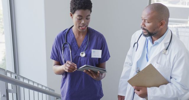 African american male and female doctors holding clipboard and tablet, talking at hospital - Download Free Stock Photos Pikwizard.com