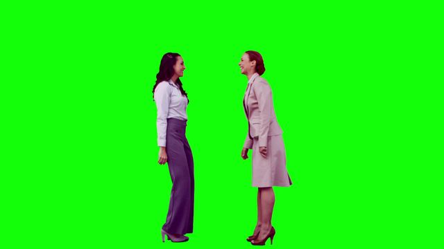 Two women in formal attire appear laughing together against a chroma key green background. This setting is ideal for editing and composite work, offering flexibility for content creators, advertisers, and designers who want to overlay the image with different themes or messages. Excellent for concepts related to joy, business networking, or positive interpersonal interactions.