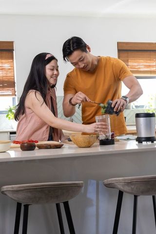 Asian couple preparing green smoothie at modern kitchen island, blending healthy lifestyle