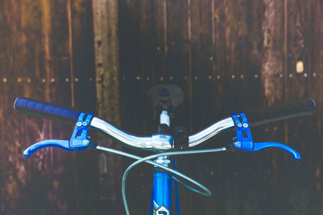 Close-up view of blue bicycle handlebars positioned against a rustic wooden background. Ideal for use in promotional materials for cycling equipment, recreational activities, or urban living. Also suitable for fitness-related content or advertisements emphasizing sustainability and eco-friendly transportation.