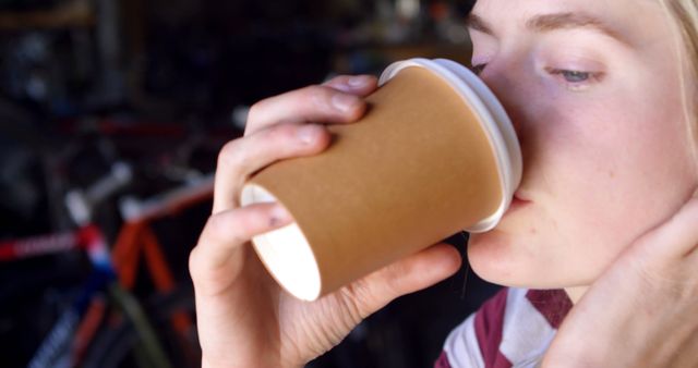 A young woman enjoys a take-out coffee, providing a moment of relaxation. Ideal for promoting coffee shops, articles on casual lifestyles, and advertisements focusing on beverages and relaxation breaks.