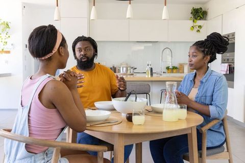 African american family conversing around modern kitchen table, sharing salad and lemonade