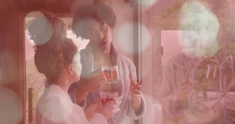Morning conversation in bathrobes sharing tea by sliding glass door with soft pink bokeh