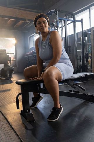 African american woman resting on gym bench wearing smartwatch and light blue activewear