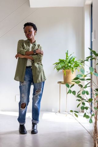 Confident african american woman standing in sunlit minimalist home wearing ripped jeans