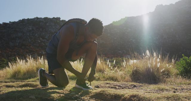 African american man exercising outdoors tying his shoe in countryside on a mountain. Fitness training and healthy outdoor lifestyle.