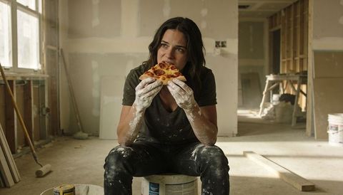 Renovation Break Woman Eating Pizza Sitting on Paint Bucket in Dusty Workroom Interior