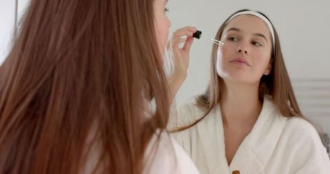 Woman Applying Serum at Bathroom Mirror for Skincare Routine