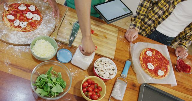 Friends gather in a kitchen, making homemade pizza with fresh ingredients like mushrooms, spinach, and cherry tomatoes. Ideal for use in articles or educational content about cooking, group activities, social gatherings, and healthy eating.