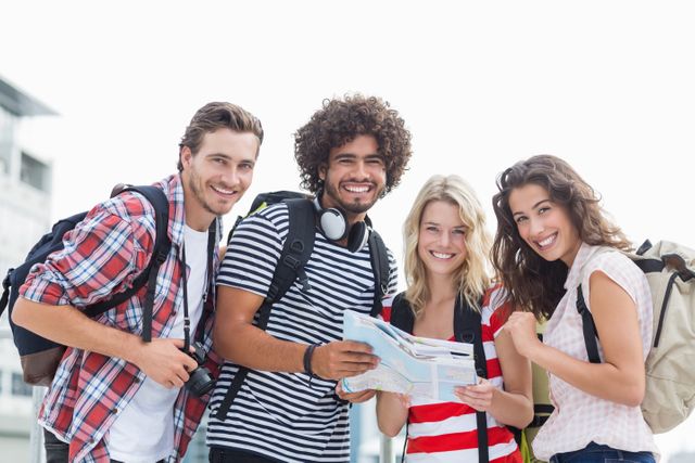 Group of cheerful friends holding a map while standing outdoors. Ideal for travel blogs, tourism advertisements, adventure planning guides, and social media posts promoting friendship and exploration.