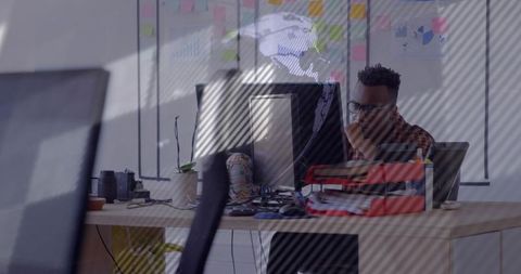 Concentrating through glass: man working at desk with computer and global data overlay