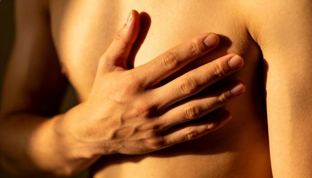 Hand pressing bare chest in warm light, closeup of male torso showing veins and skin texture