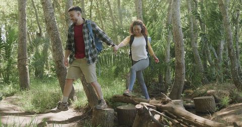 Joyful Mixed Couple Hiking in Sunny Forest Holding Hands