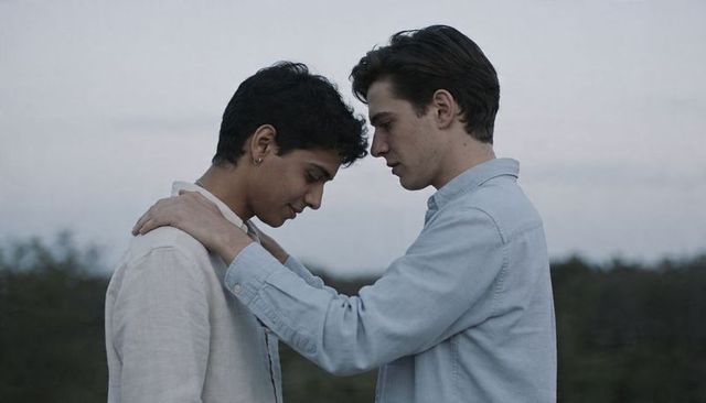 Two young men sharing tender moment at dusk, foreheads touching, pale-blue and linen shirts