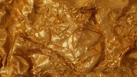 Macro video gold foil crinkling and reflecting studio light, glitter flecks shimmering