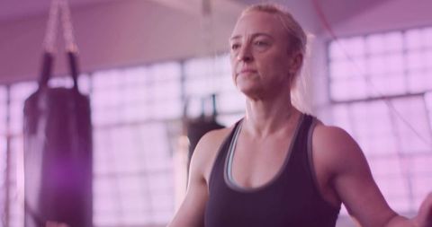 Focused middle-aged woman training boxing drills in bright gym with heavy bag