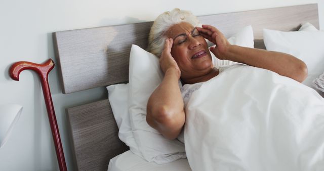 Sick african american senior woman holding her head while lying on the bed at home - Download Free Stock Photos Pikwizard.com