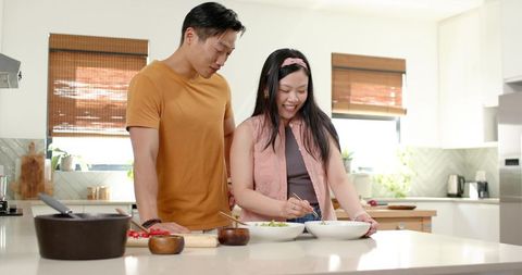 Asian couple cooking together at bright modern kitchen island preparing fresh healthy meal