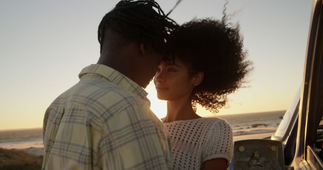 An affectionate couple is embracing near the ocean during sunset, their heads close together and smiling warmly. This image can be used to represent love, romance, and togetherness. Ideal for relationship counseling, dating services, travel brochures, or love-themed marketing campaigns.