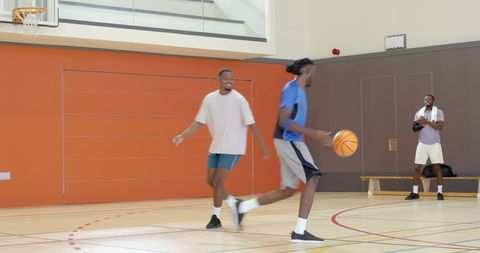 Men playing basketball on indoor court dribbling and defending during informal pickup game