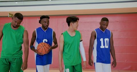 Four basketball players walking on indoor court in green and blue jerseys showing teamwork