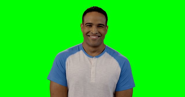 Man wearing casual shirt with blue sleeves on green screen background, smiling happily. Ideal for diverse marketing campaigns, promotional materials, social media, and video editing requiring green screen effects.
