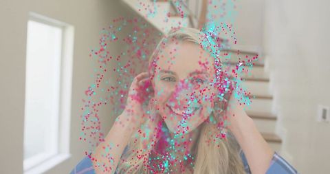 Smiling mid-adult woman celebrating with pink and cyan confetti on bright home staircase
