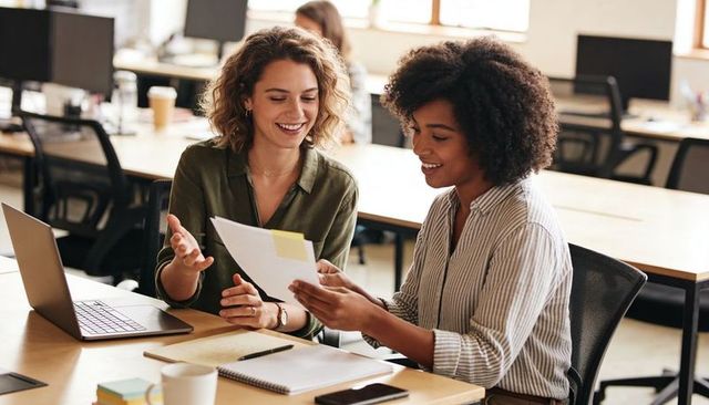 Collaborating colleagues reviewing document, planning strategy at modern open-plan office desk
