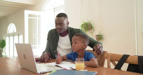 African american father guiding son with homework on laptop at home