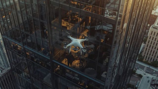 Hovering drone filming glass facade of high-rise revealing diners in business lounge at golden hour