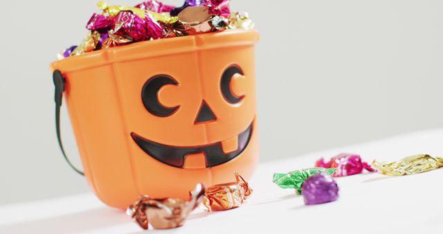 Halloween-themed pumpkin bucket overflowing with vibrant candies. Ideal for holiday promotions, festive advertisements, and children's activities. Perfect for social media posts, marketing materials, or creating a spooky atmosphere in seasonal campaigns.