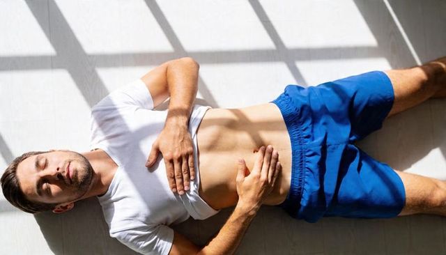 Sunlit man resting on floor with window grid shadows wearing white tee and blue shorts