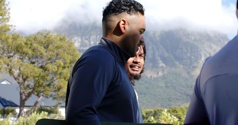 African american friends carrying green board near mountain homes wearing jackets