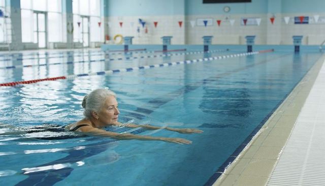Senior woman swimming laps in indoor pool for fitness healthy aging