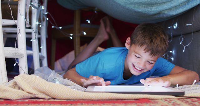 Caucasian boy smiling while using digital tablet under the blanket fort at home. family, love and togetherness concept