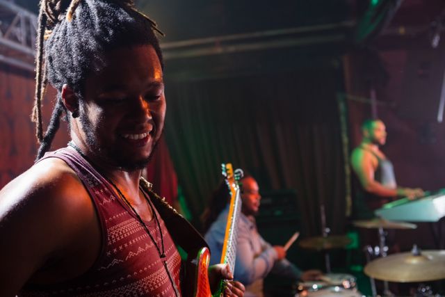 Guitarist playing guitar on stage in a nightclub with band members in the background. Ideal for use in articles about live music, nightlife, entertainment, and concert events. Suitable for promoting music venues, bands, and musical performances.
