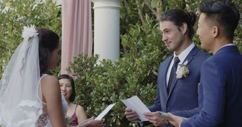 Groom sharing vows with smiling bride in romantic outdoor ceremony