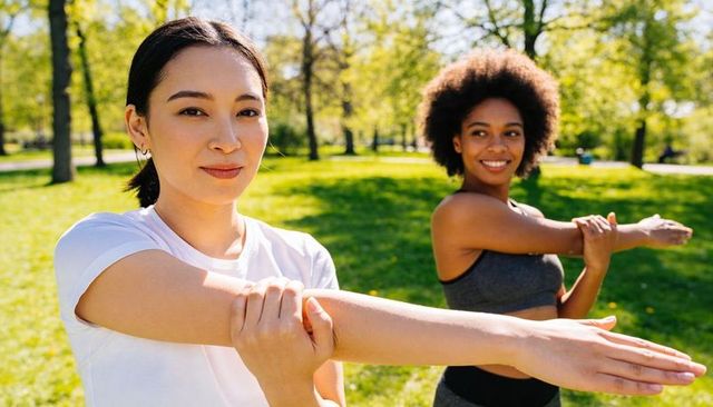 Women stretching arms in sunny park warming up for outdoor run and fitness training