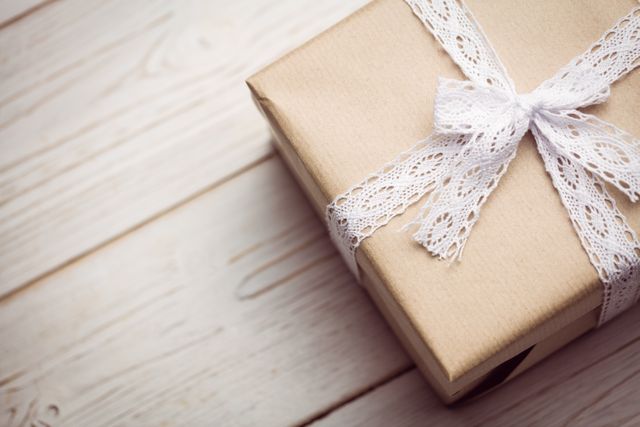 Brown gift box wrapped with white lace ribbon on light wooden floor. Perfect for use in holiday, birthday, or anniversary promotions, gift wrapping tutorials, or vintage-themed decor ideas.