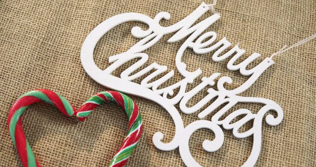 A festive Merry Christmas sign in elegant cursive is accompanied by a candy cane heart on a burlap background, with copy space. These holiday decorations evoke the warmth and joy of the Christmas season.