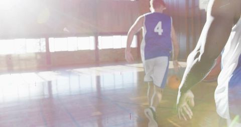 Running basketball player wearing blue jersey number 4 driving downcourt in sunlit gym