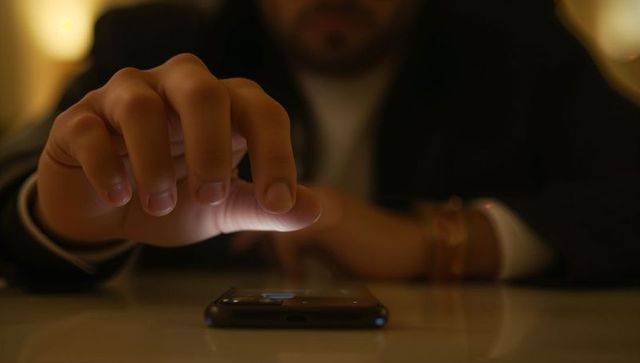 Reaching hand touching smartphone on reflective table night lounge warm glow moody
